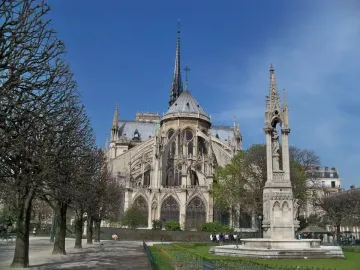 Fontaine de la Vierge monument in front of Notre-Dame Cathedral with its spire and flying buttresses.