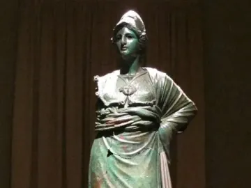 Minerva d\'Arezzo, a green-patinated armored figure standing on a wooden pedestal against a dark backdrop.