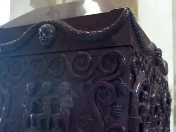 Sarcophagus of Constantina with carved reliefs of figures, garlands, and grapevines on a dark red stone surface.