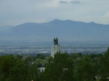 This Is the Place Monument framed by trees with Salt Lake Valley and distant mountains beyond.