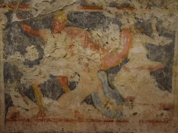 Weathered painted fragment from the Amazon Sarcophagus showing faded figures in red, orange, white, and blue.