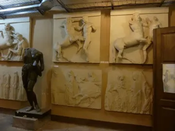 Parthenon metope relief panels showing damaged mythological battle scenes, with a dark headless statue in the foreground.