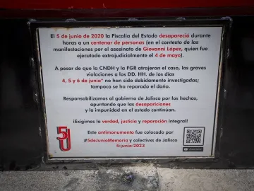 Close-up of the Antimonumento 5J metal plaque with Spanish text and a QR code.