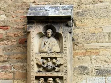 Weathered stone relief of the Tomb of Bruno the Priest, showing stacked figural scenes and vertical inscriptions on a wall.