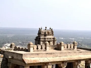 A multi-tiered stone shrine overlooking a hazy green landscape under a clear sky.