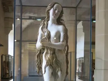 Mary Magdalene sculpture of a standing female figure with long wavy hair, displayed in a glass case.
