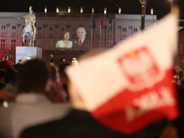 The Prince Józef Poniatowski Monument lit in red at night in front of a grand building with projected images on its facade.