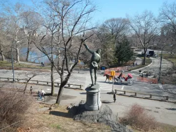 The Falconer bronze statue seen from behind, standing on a stone pedestal with one arm raised.