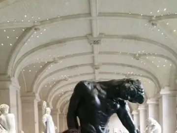 The Shade sculpture by Rodin in a museum hall, with a person posing beside it in a similar bent-forward stance.