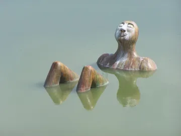 Hombre Río sculpture emerging from calm water with a peaceful face.