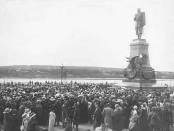 The Monument of Alexander III stands on a decorated multi-tiered pedestal with a large crowd gathered around it.