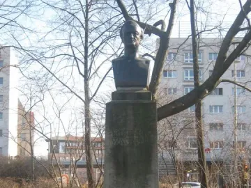Richard Wagner bust on a weathered stone pedestal with a floral wreath at the base in a park