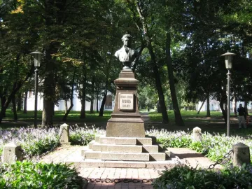 Bronze bust of Pushkin on a dark pedestal in a misty park.