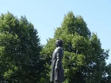 Pushkin statue on a tall pedestal in a park with trees and blue sky behind it.
