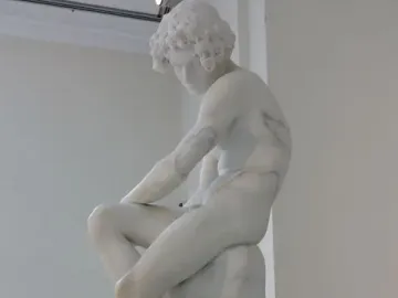 The Exiled, a white marble sculpture of a bowed youthful figure seated on rock.
