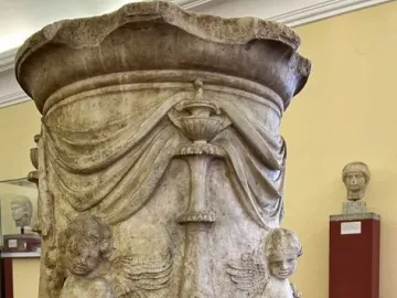 Four Seasons Altar with carved reliefs, a central vessel, and two winged figures on a textured stone base.