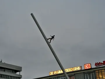 The Man Walking to the Sky sculpture rises on a tilted pole in a plaza in front of the main station buildings.