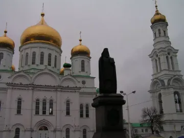 Monument to Dimitry of Rostov in front of a white Orthodox cathedral with golden domes and a bell tower.