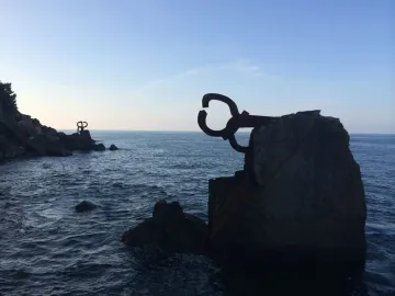 Peine del Viento sculptures silhouetted on rocky coastline beside a dark, choppy sea