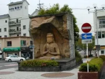 Usuki Stone Buddha seated in a carved grotto structure in a paved urban square.