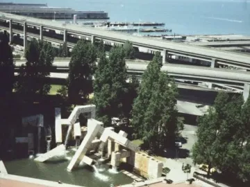 Vaillancourt Fountain in a plaza with concrete blocks and water, with trees and freeway overpasses in the background.
