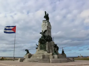 Antonio Maceo Monument with bronze figures and an equestrian statue at the top, with a Cuban flag and the sea behind it.