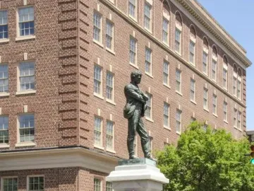 Appomattox bronze statue of a man with crossed arms on a tall stone pedestal at a street intersection.
