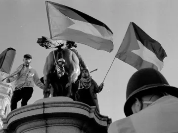 Rear view of the Duke of Cambridge equestrian statue with several people on the pedestal holding flags.