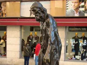 Eustache de Saint Pierre bronze sculpture of a bearded man in long robes standing on a stone base beside storefront windows