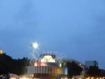 Fire and Water Fountain illuminated in a city square at dusk, with colorful vertical panels and arcing water jets.