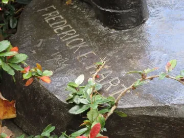 Close-up of the Frederick F. Hart inscription on the dark, textured base of The Three Soldiers, partly covered by thorny foliage and red berries.