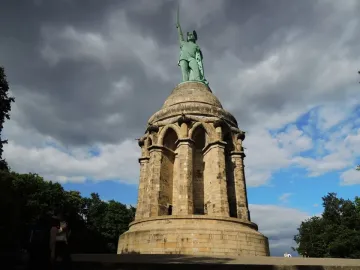 Hermannsdenkmal monument with a warrior statue holding a sword aloft against a dramatic cloudy sky.