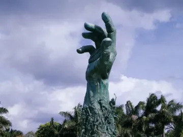 Holocaust Memorial sculpture in Miami Beach, a dark green raised arm and open hand rising above smaller figures and water.