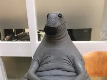 Homunculus Loxodontus sculpture wearing a black face mask and resting its clasped hands on its belly.