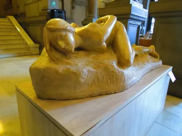 Malgré Tout, a stone sculpture of a reclining woman with flowing hair on a wooden pedestal.