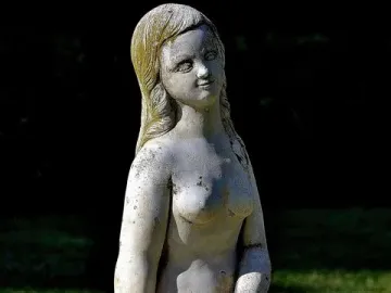 Weathered stone mermaid fountain statue with water flowing from the figure\'s hands.