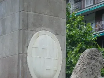 Close-up of the Fountain of Hercules showing a carved lion head spouting water beside a marble plaque and stone lion sculpture.