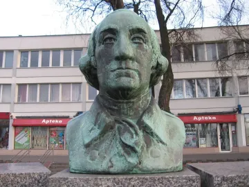 Teal-patinated bust of George Washington with a building and Apteka storefront behind it.