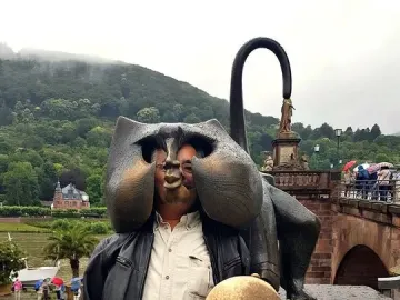 Person posing behind the Heidelberg Bridge Monkey sculpture with their face placed in the hollow head opening.