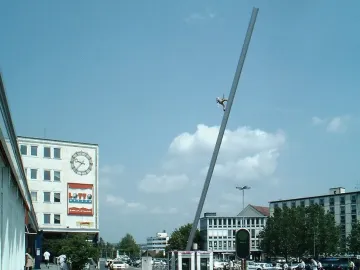Himmelsstürmer sculpture on a tilted pole against a blue sky above an urban square in Kassel
