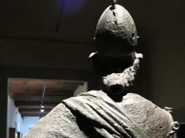 Rear view of Minerva d\'Arezzo showing the crested helmet, detailed hair, and draped clothing with a green and brown patina.