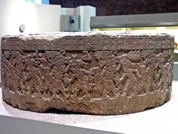 Stone of Motecuhzoma I with a carved cylindrical frieze of figures in elaborate headdresses.