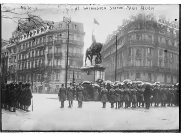 Crowd with umbrellas gathered before the Washington statue in a rainy square lined with ornate buildings.