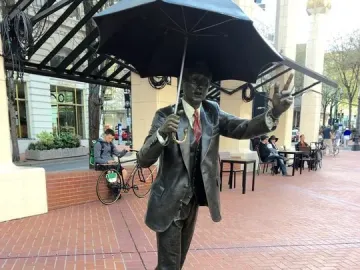 Allow Me, a dark bronze sculpture of a man in a suit holding a large umbrella and raising one hand.