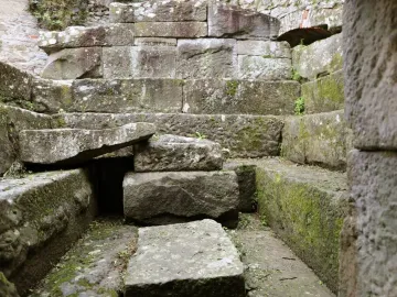Weathered stone blocks and a slanted slab inside an Etruscan tomb ruin, with patches of green moss.