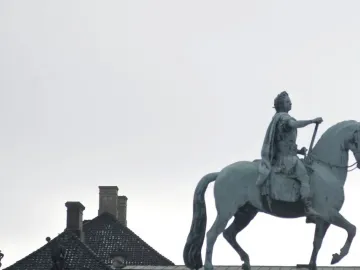 Frederick V equestrian statue in bronze against an overcast sky, with rooftops below.