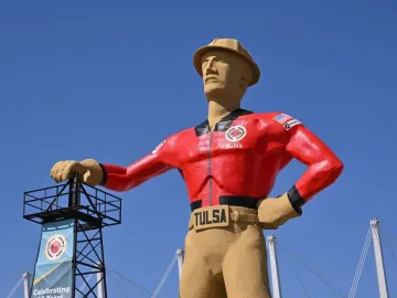 Golden Driller statue in Tulsa wearing a red jacket and tan hard hat beside a black metal tower.