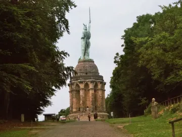 Hermannsdenkmal, a green-patina warrior statue holding a sword high atop a stone pedestal with arched openings, surrounded by trees.