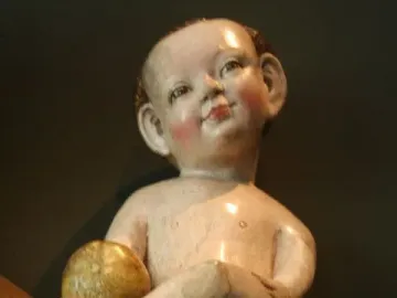 Rosy-cheeked baby figure holding a golden orb on a dark textured surface.