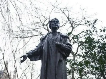 Pankhurst Memorial statue on a tiered stone pedestal, with the figure’s arm outstretched outdoors among bare trees.